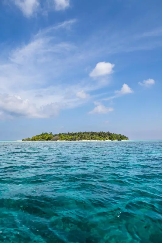 Une île tropicale bordée d'une eau turquoise et d'une plage de sable blanc sous un ciel bleu nuageux.