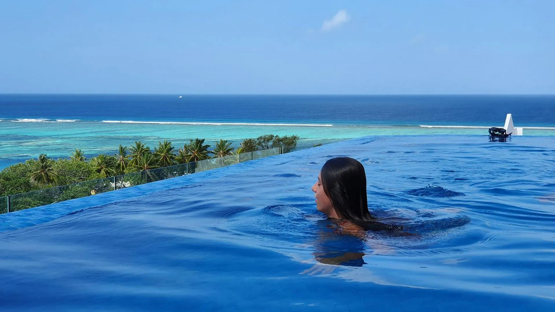Une femme se tient dans une piscine à débordement avec vue sur la mer.