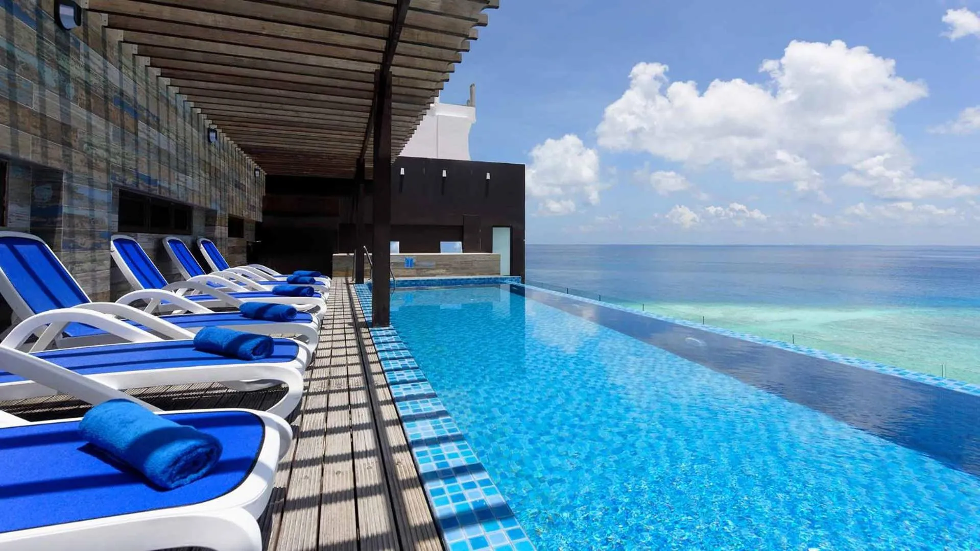 Transats bleus alignés au bord d'une piscine à débordement avec vue sur la mer.