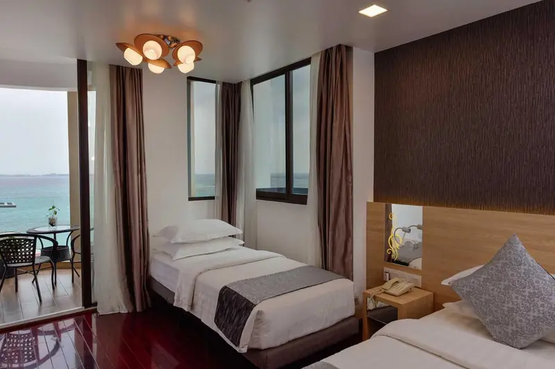 Chambre avec deux lits simples et vue sur la mer depuis un balcon.