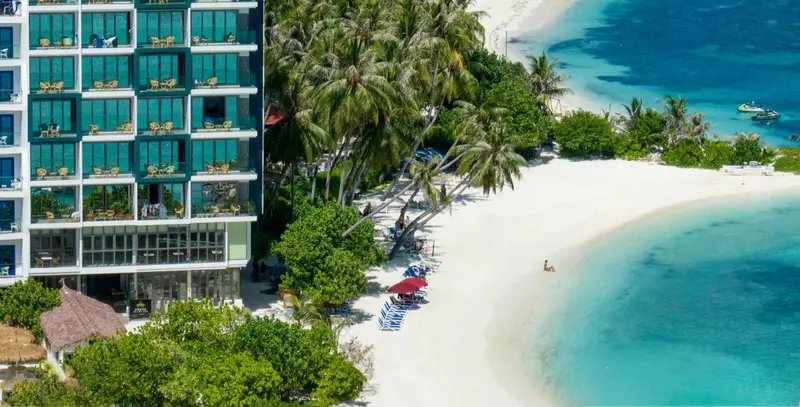 Vue aérienne d'un bâtiment turquoise bordant une plage de sable blanc et une mer turquoise.