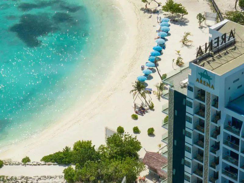 Vue aérienne d'une plage de sable blanc bordée d'une eau turquoise et d'un bâtiment moderne.