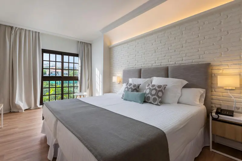 Une chambre lumineuse avec un grand lit et un mur en briques blanches.
