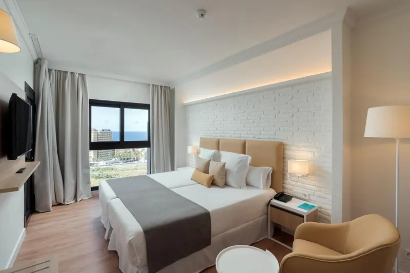 Une chambre lumineuse avec un grand lit et un fauteuil.