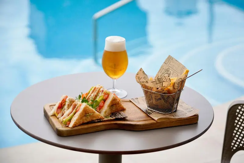 Un sandwich et des frites sont servis sur une table près d'une piscine.