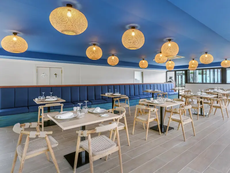 Une salle lumineuse avec des tables dressées et des suspensions en rotin.