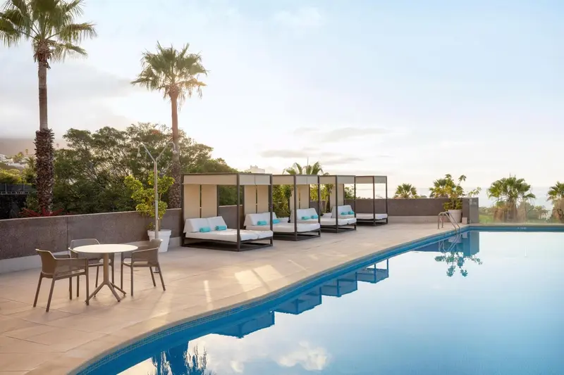 Transats et table basse au bord d'une piscine ensoleillée.