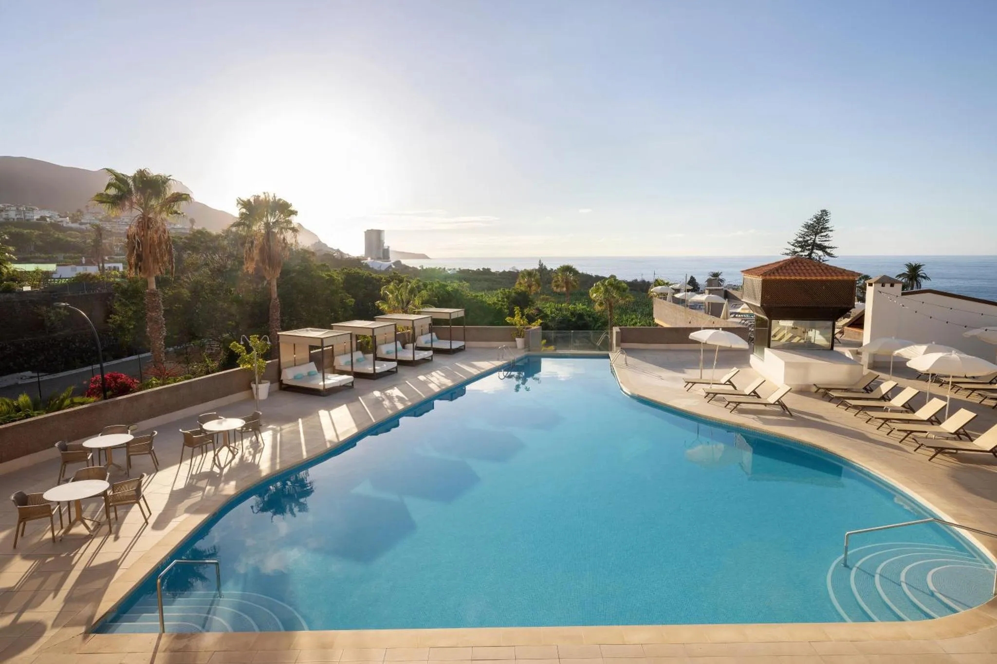 Une piscine avec des transats et des parasols offre une vue sur la mer et les montagnes.