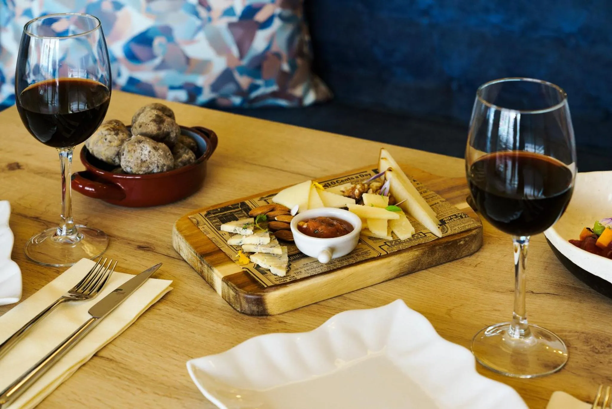 Une table en bois présente des verres de vin rouge, une sélection de fromages et des amuse-gueules.