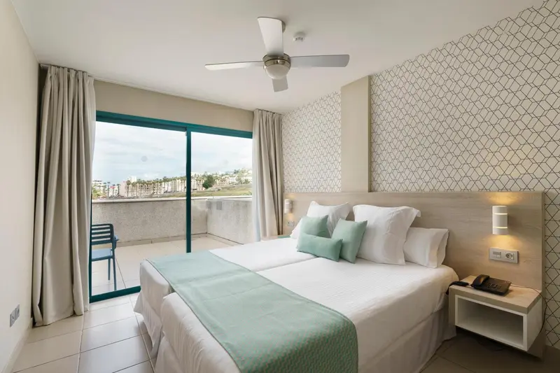 Une chambre lumineuse avec un grand lit et un accès à un balcon.