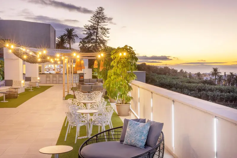 Terrasse aménagée avec mobilier de jardin et vue sur la mer au coucher du soleil.