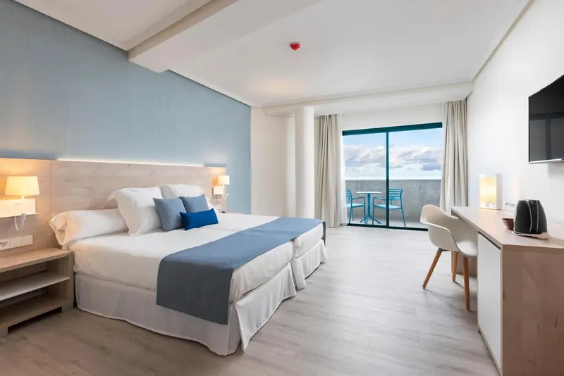 Chambre lumineuse avec un grand lit et un accès à une terrasse.
