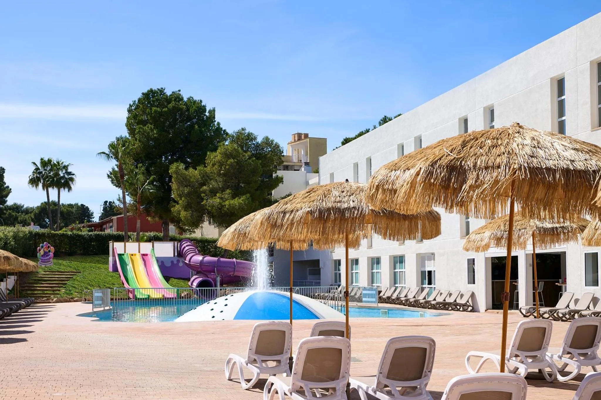 Transats et parasols à l'ombre près d'une piscine avec toboggans.