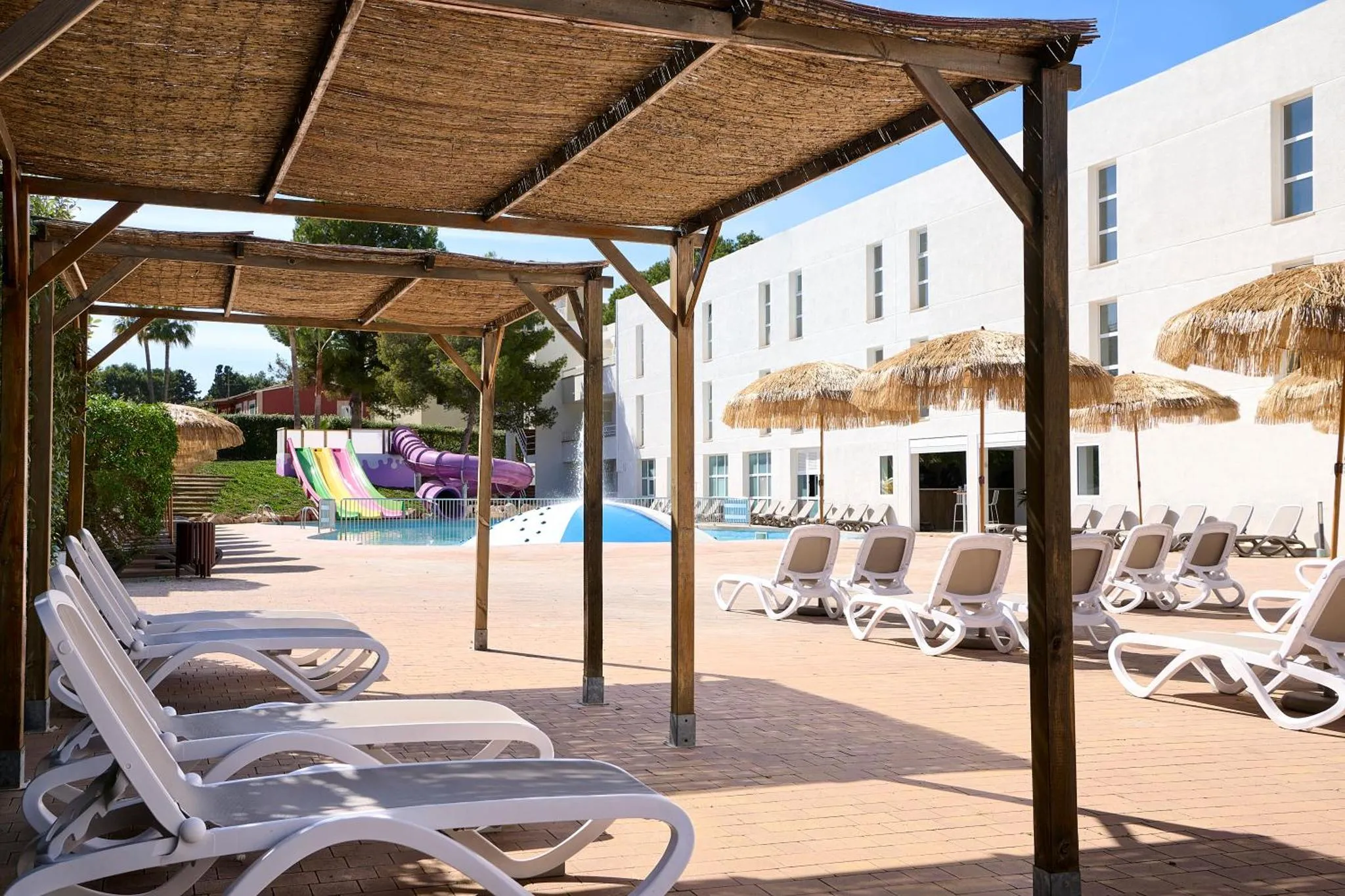 Terrasse ombragée avec transats et piscine en arrière-plan.