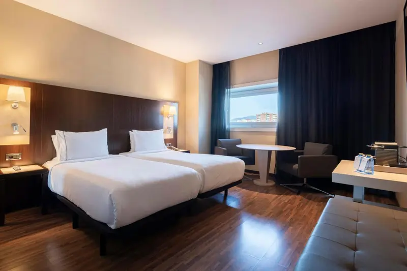 Une chambre d'hôtel lumineuse avec deux lits simples et un coin salon.