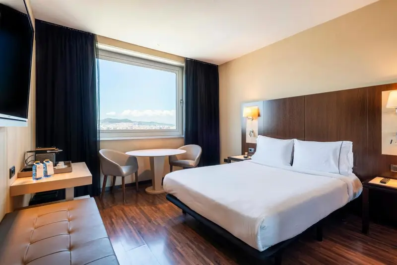 Chambre d'hôtel moderne avec un lit double et un coin salon près d'une fenêtre.