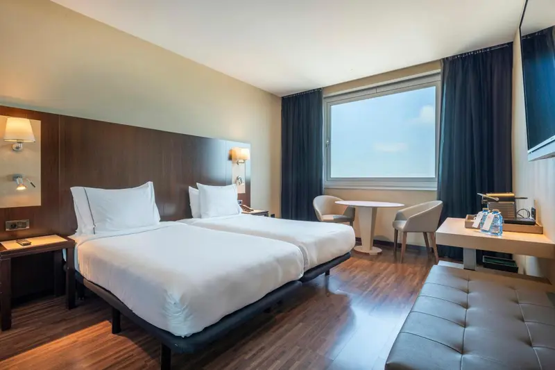 Une chambre d'hôtel lumineuse avec deux lits simples et un coin salon.