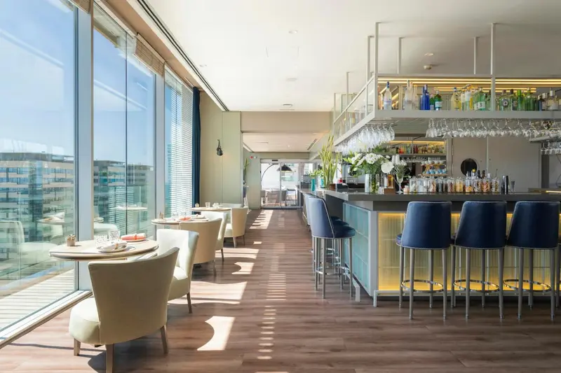 Un bar lumineux offre une vue sur la ville depuis de grandes baies vitrées.