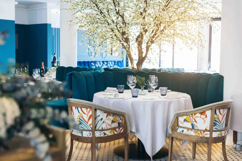 Une table ronde dressée dans une salle lumineuse avec des banquettes vertes et des fleurs.