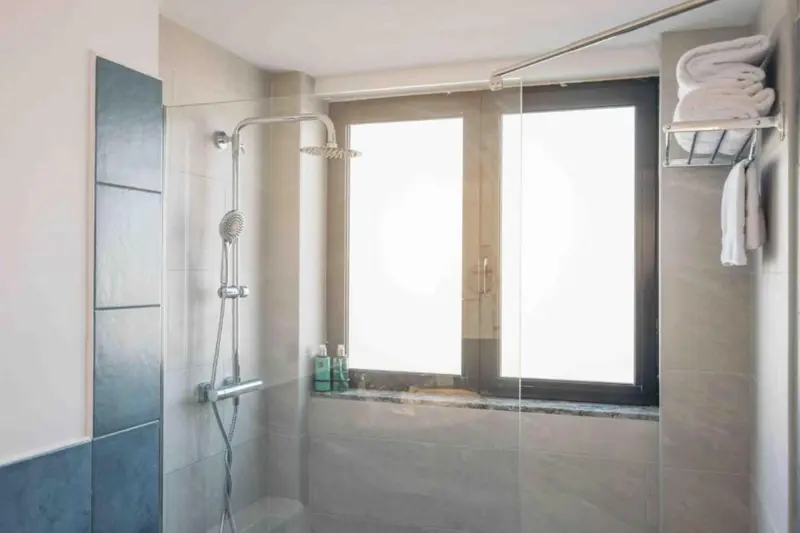 Une douche à l'italienne moderne avec des carreaux bleus et une fenêtre.