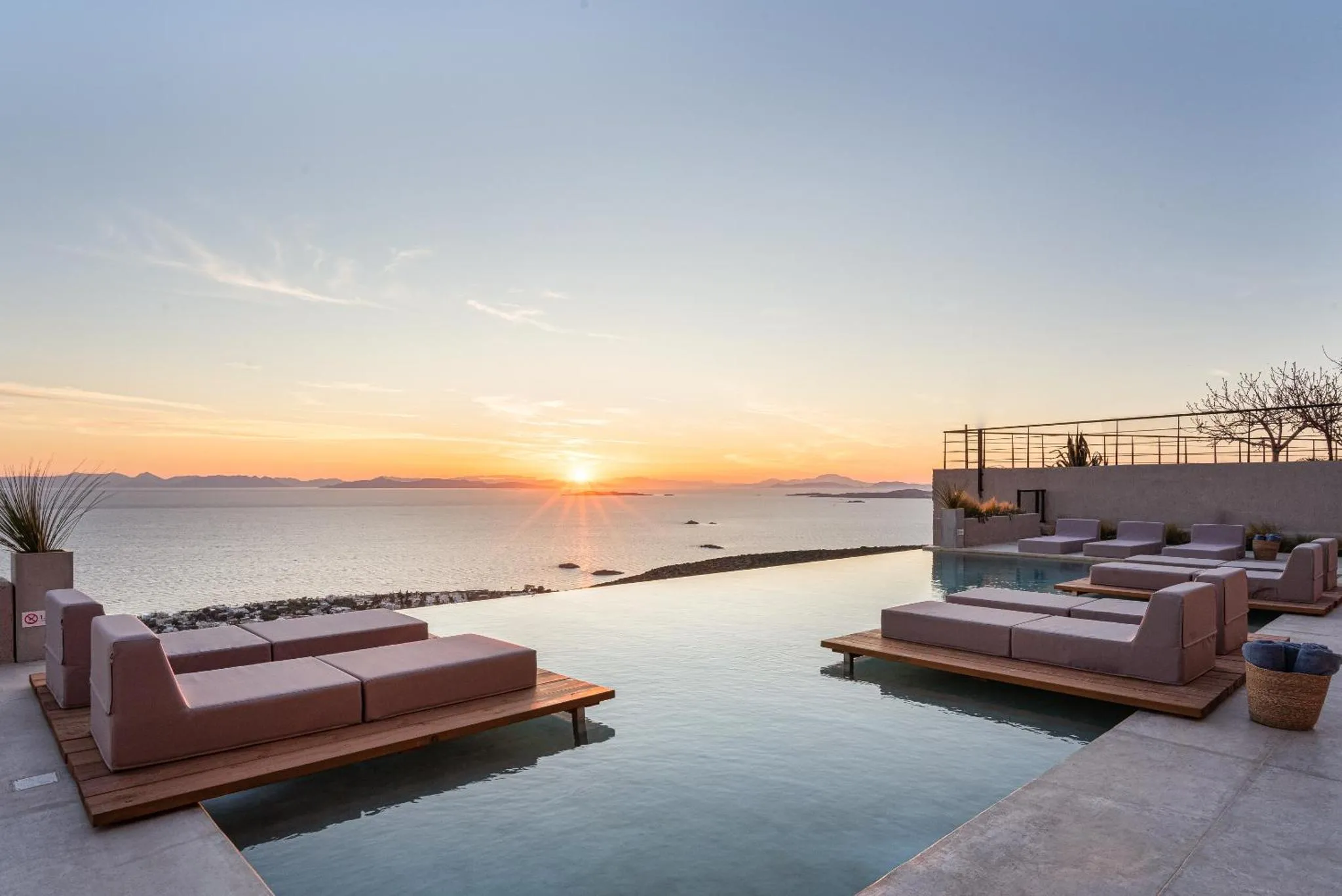 Transats et piscine à débordement face à la mer au coucher du soleil.