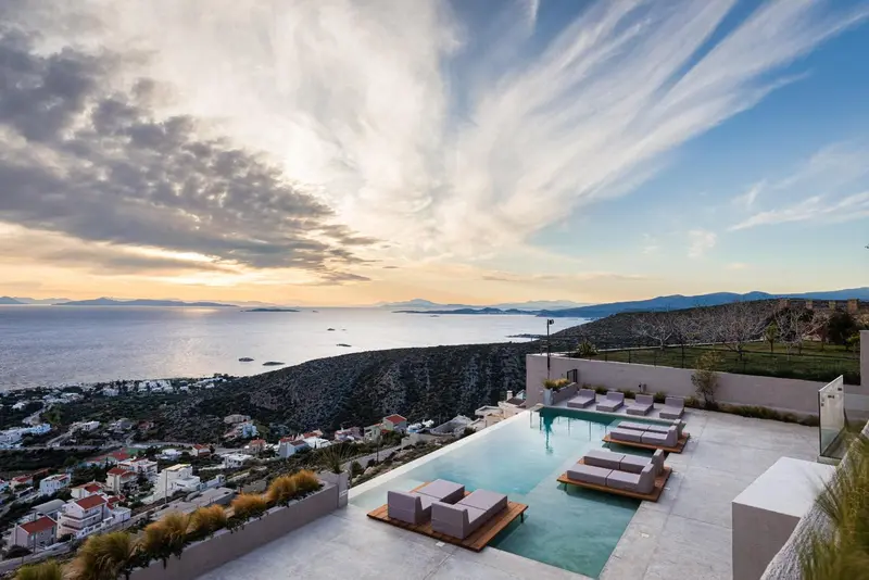 Une piscine à débordement offre une vue sur la mer et les collines environnantes au coucher du soleil.