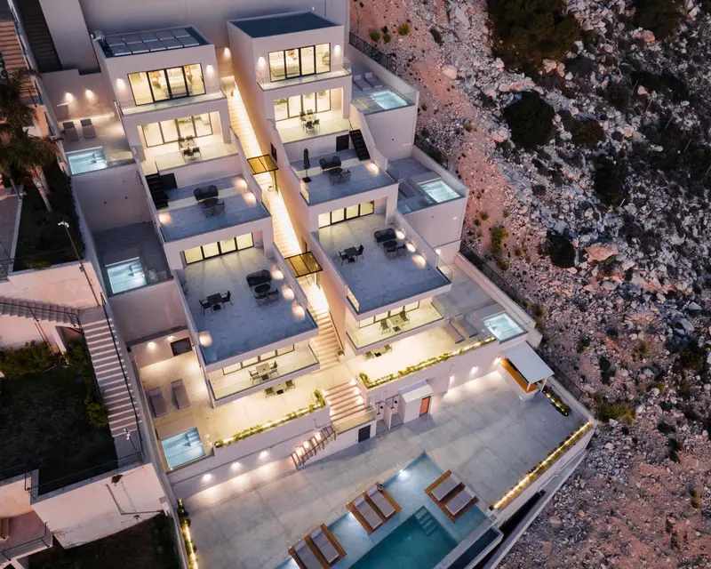 Vue aérienne d'un bâtiment moderne illuminé avec des terrasses et une piscine.