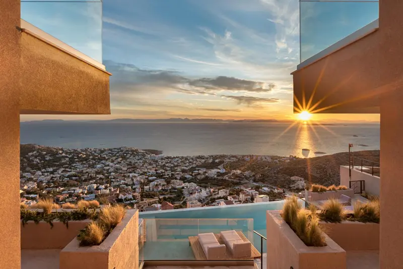 Vue sur la mer et le soleil couchant depuis une terrasse avec piscine.