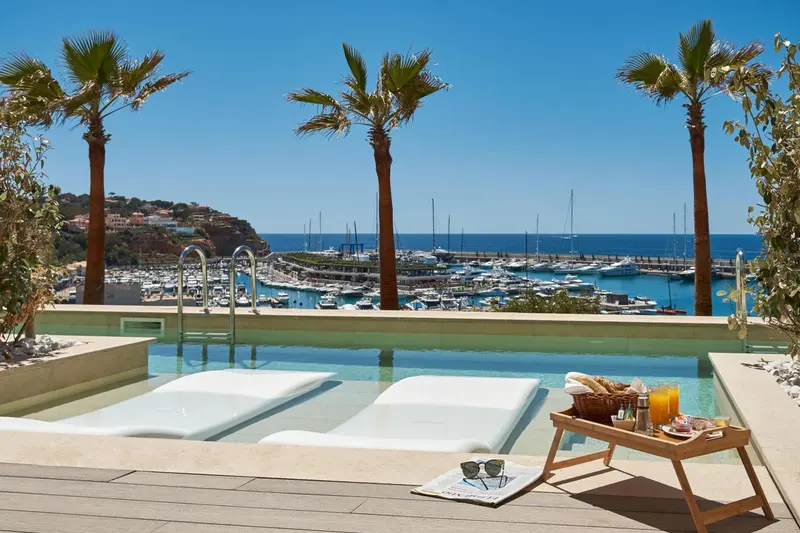 Deux transats blancs bordent une piscine à débordement avec vue sur un port de plaisance ensoleillé.