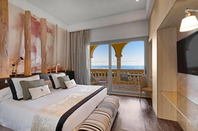 Chambre moderne avec un grand lit et une vue sur la mer depuis un balcon.