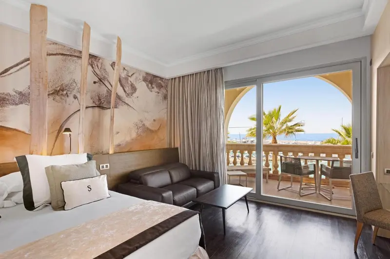 Chambre avec un lit double, un canapé et une vue sur la mer depuis un balcon.