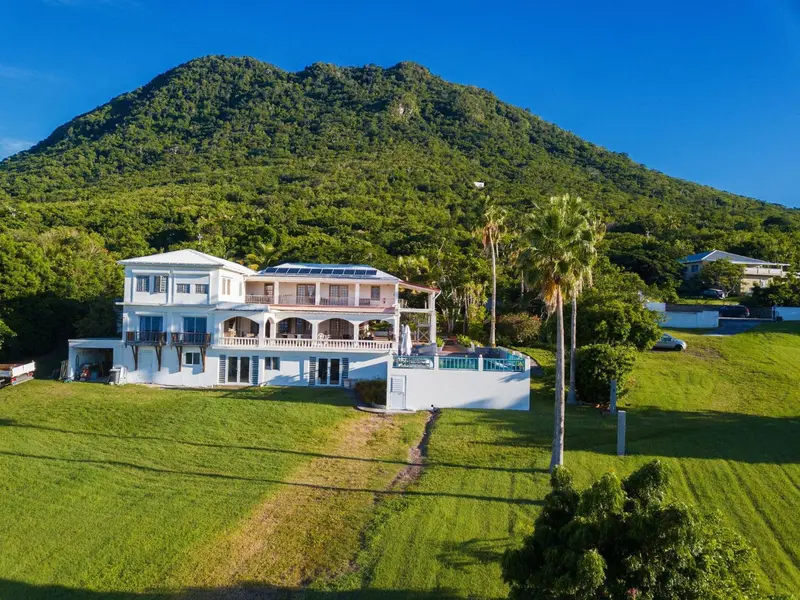 Vue aérienne d'une résidence blanche avec une piscine et une végétation luxuriante en arrière-plan.