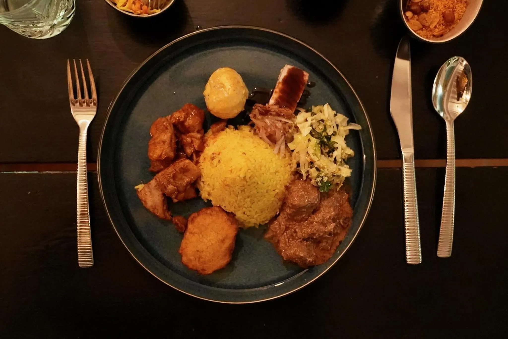 Assiette garnie de divers plats et couverts sur une table sombre.