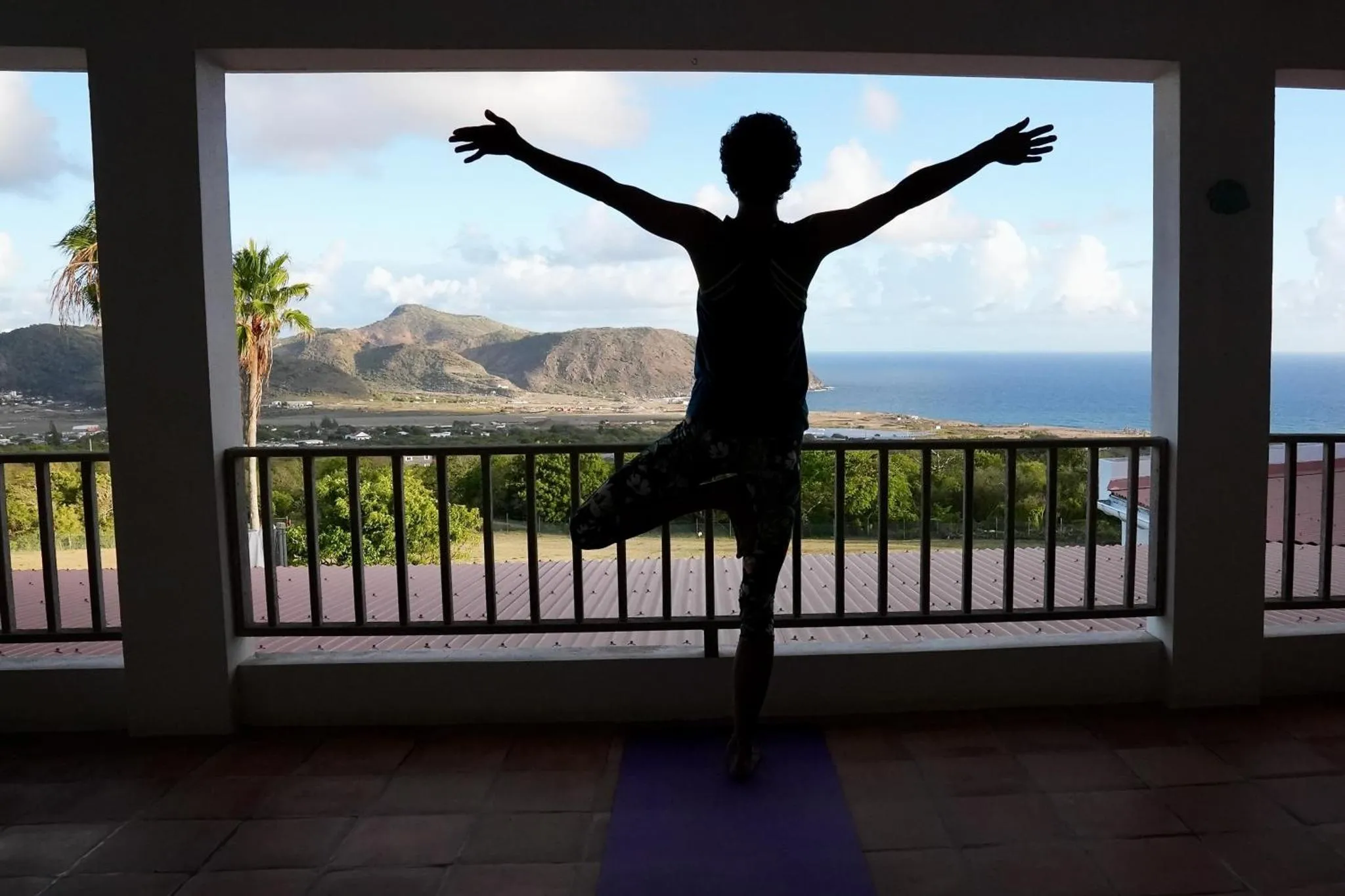 Silhouette d'une personne pratiquant le yoga sur une terrasse avec vue sur la mer.