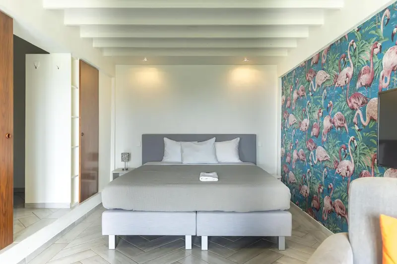 Une chambre lumineuse avec un grand lit et un mur décoré de flamants roses.