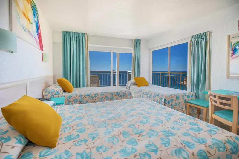 Chambre lumineuse avec deux lits simples et un lit double, vue sur la mer.