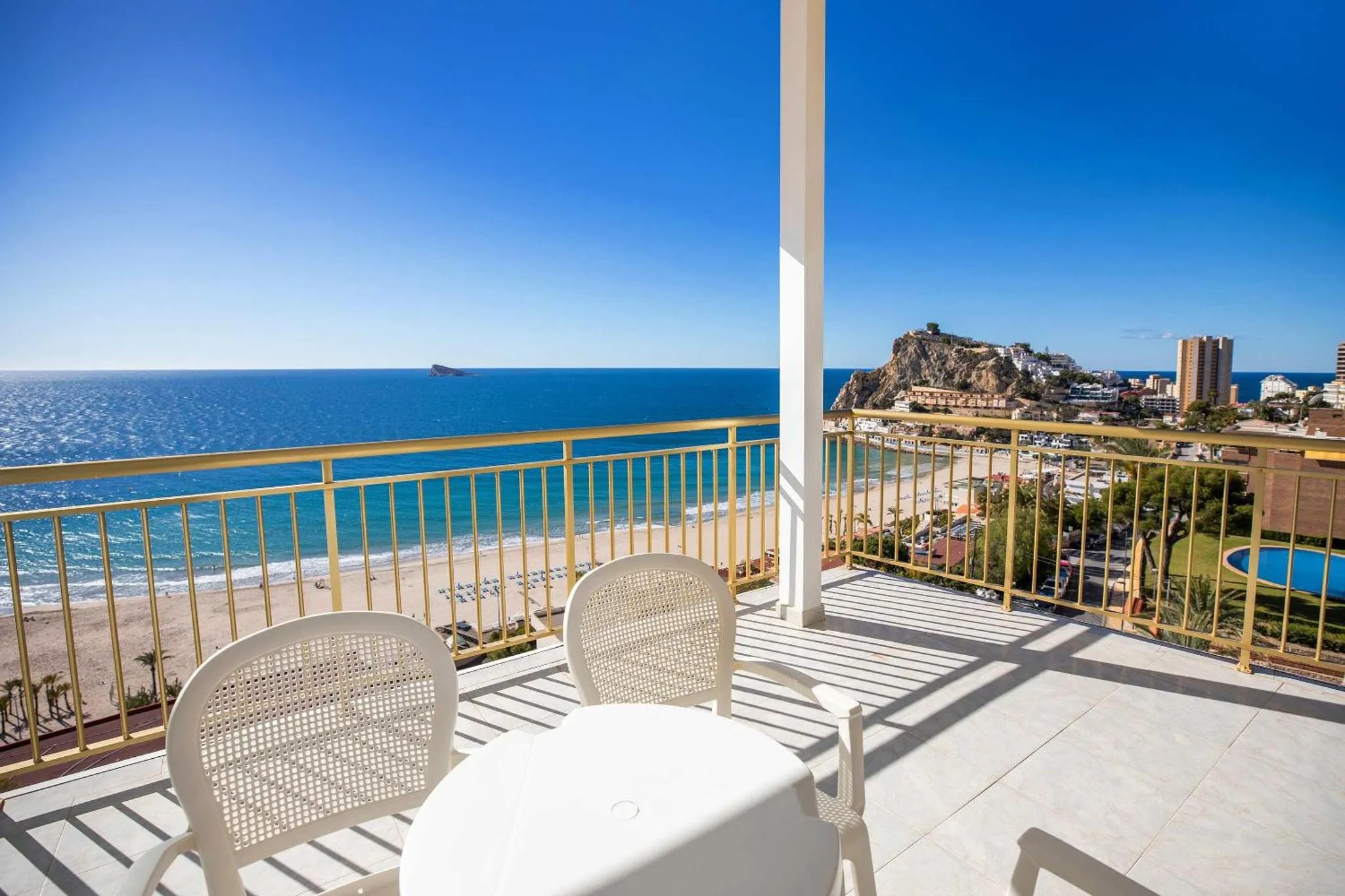 Vue d'une terrasse avec mobilier blanc donnant sur la mer et une plage.