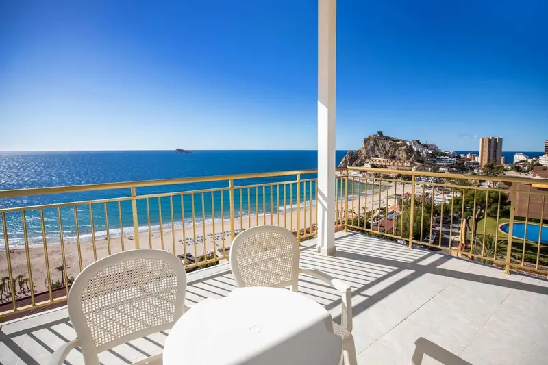 Vue d'une terrasse avec mobilier blanc donnant sur la mer et une plage.