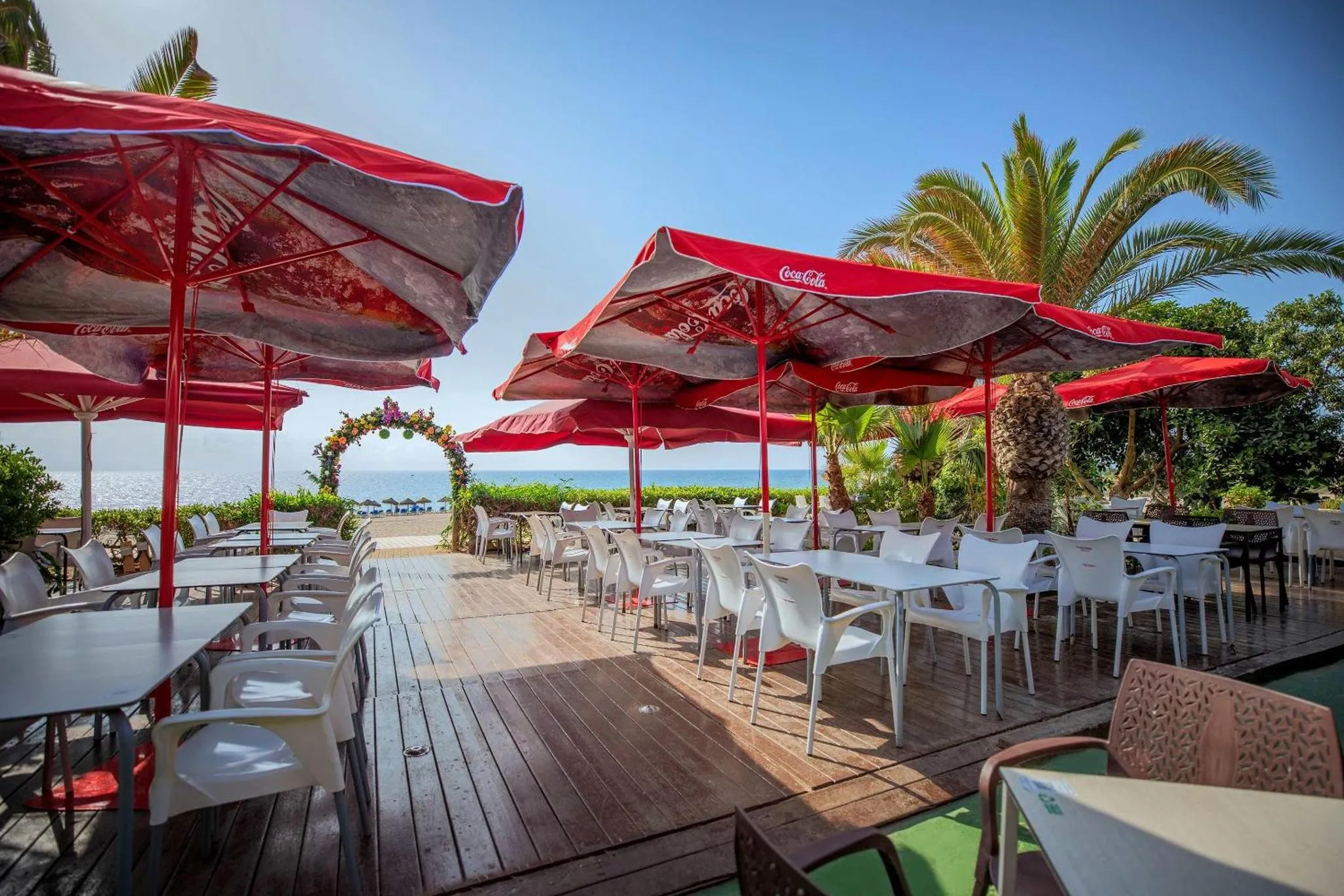 Terrasse ombragée avec tables et chaises en plastique donnant sur la mer.
