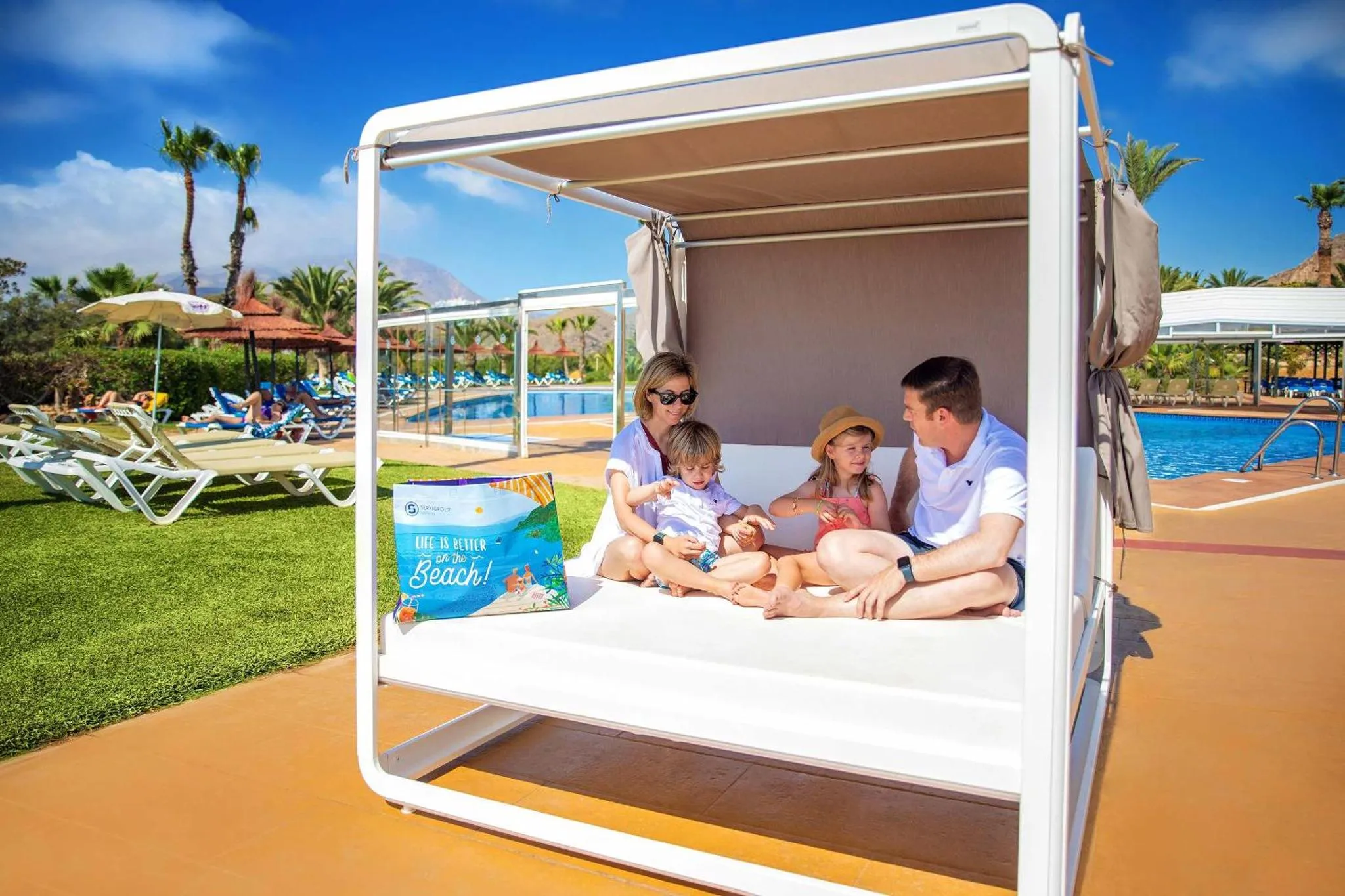 Une famille se détend sur un lit de plage ombragé près d'une piscine.