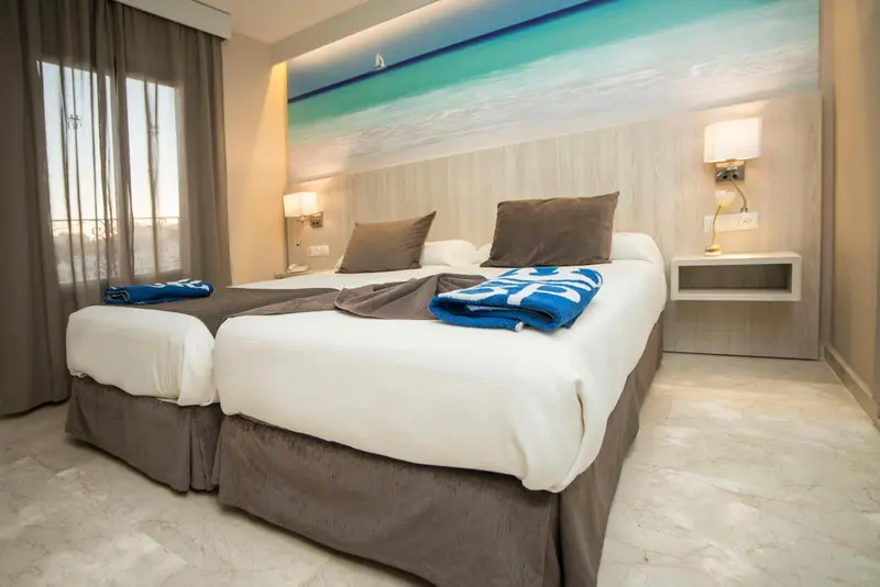 Une chambre lumineuse avec un grand lit et un décor mural évoquant la mer.