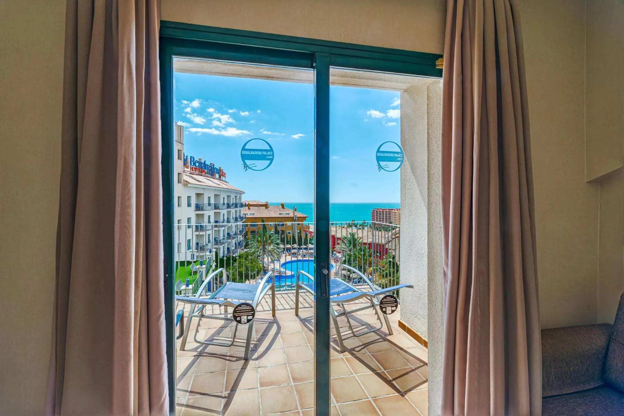 Vue sur une terrasse avec des transats et une piscine depuis une chambre.