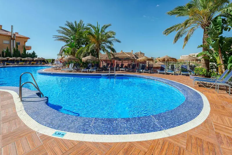 Piscine rectangulaire bleue bordée d'une terrasse en bois et de mosaïques.