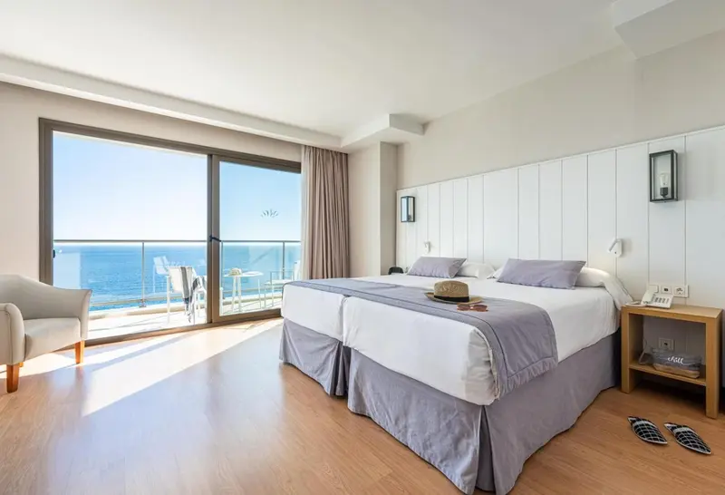 Chambre lumineuse avec un grand lit et vue sur la mer.