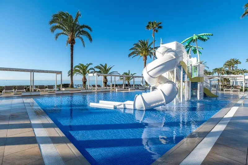 Une piscine avec un toboggan aquatique et des palmiers en arrière-plan.