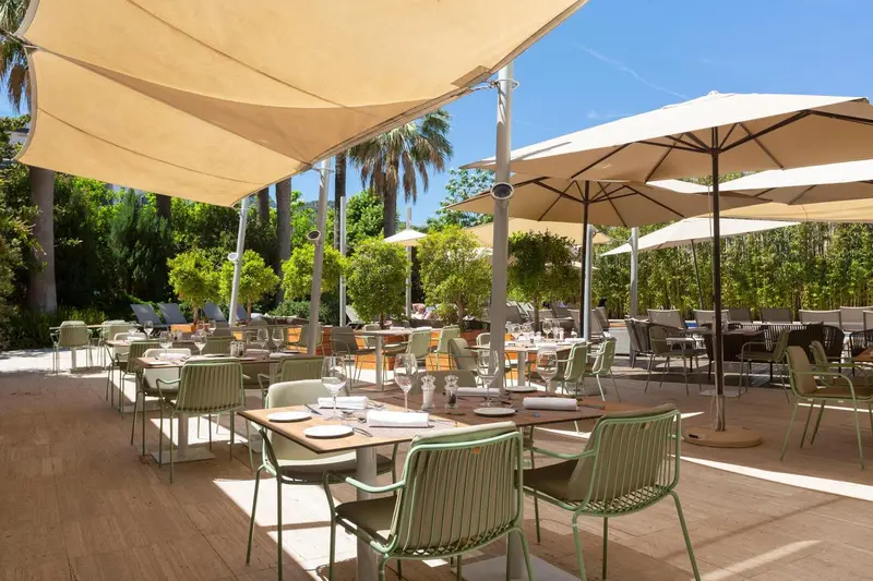 Tables et chaises vertes disposées sur une terrasse ombragée avec des parasols.
