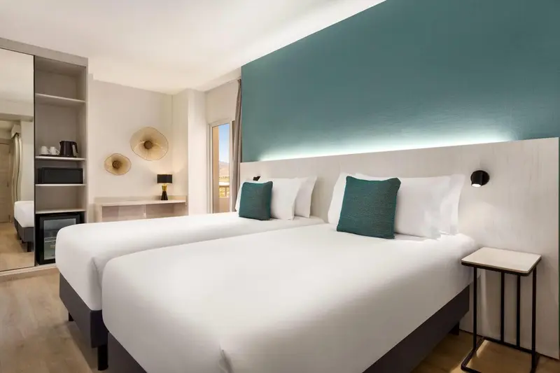 Une chambre lumineuse avec un grand lit et un mur turquoise.