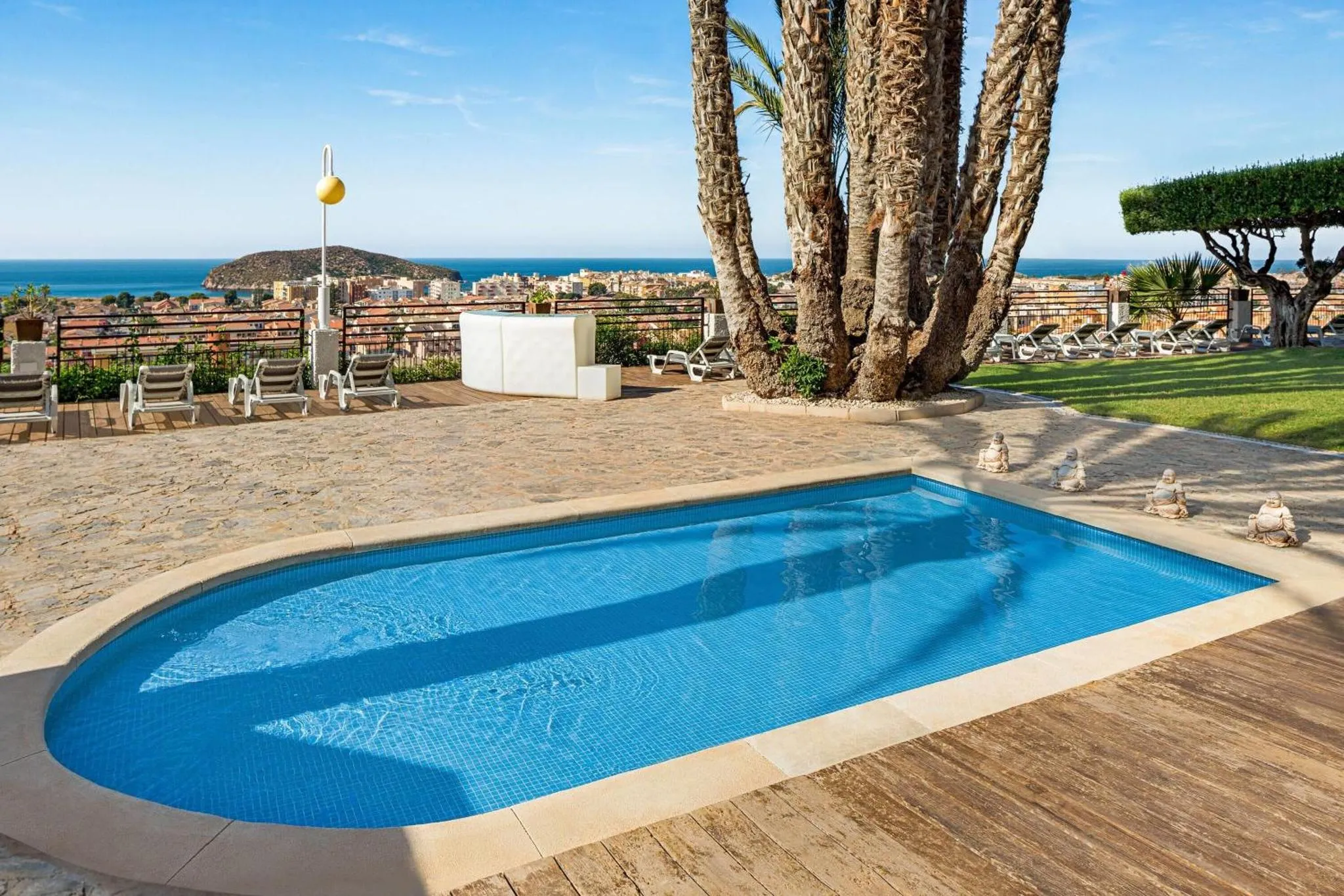 Petite piscine rectangulaire avec terrasse ensoleillée et vue sur la mer.