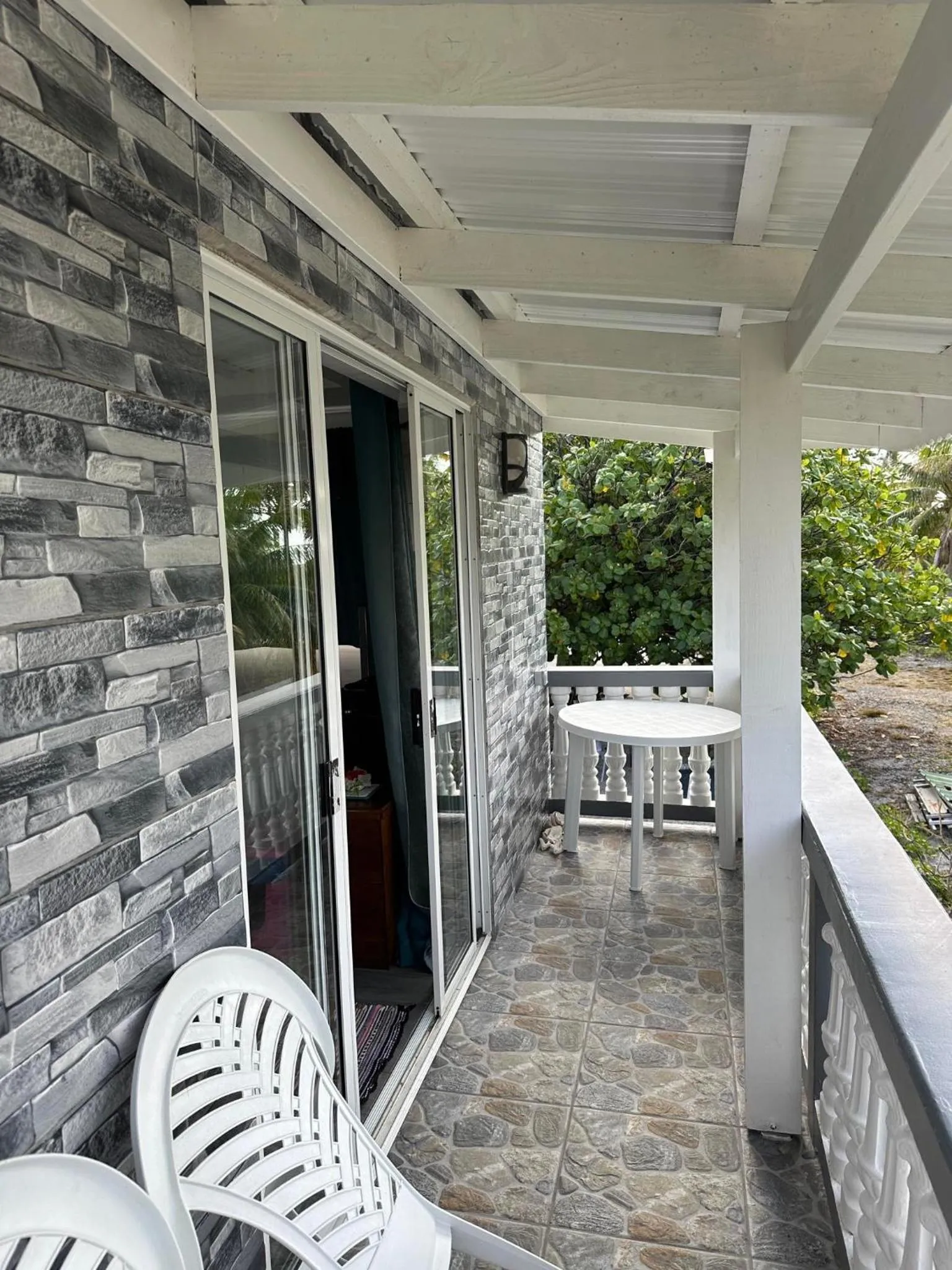 Terrasse couverte avec mobilier blanc et porte vitrée ouverte sur une pièce.