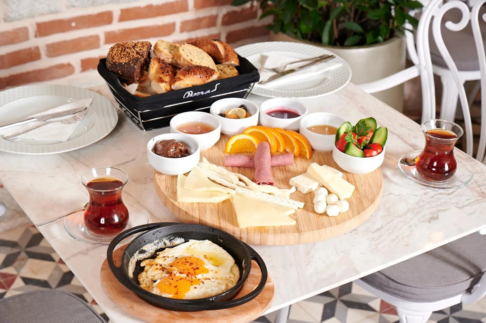 Une table est dressée avec un copieux petit-déjeuner composé de viennoiseries, de fruits, de fromages et d'œufs.